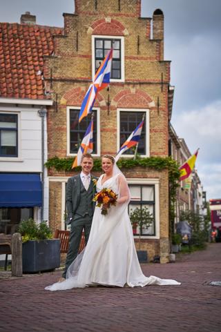 Karlijn en Glenn poseren trots voor hun trouwfoto voor het historische gebouw met Nederlandse vlaggen in Vierpolders - Trouws