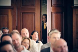 Bruidegom Gerrit verschijnt achter houten deuren tijdens ceremonie in Stadhuis Rotterdam terwijl gasten wachten - Trouwshoot