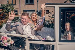 Bruidspaar Jordy en Jacky wuift blij vanuit open auto op Wantij Paviljoen in Dortrecht - Trouwshoot Stefan Segers