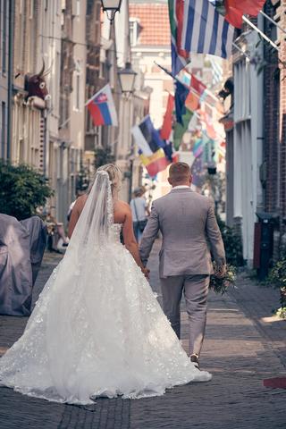 Bruidspaar Jacky en Jordy loopt hand in hand door festive straat met vlaggen, trouwreportage Wantij Paviljoen Dortrecht - Tro