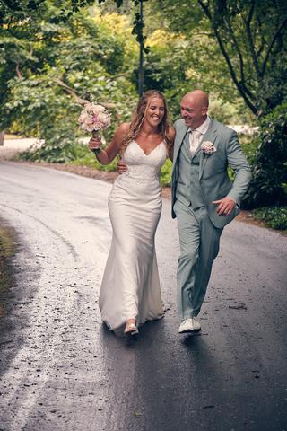 Bruidspaar Dennis en Kim loopt hand in hand door groene laan, bruidboeket roze rozen, trouwreportage Kasteel De Hooge Vuursch