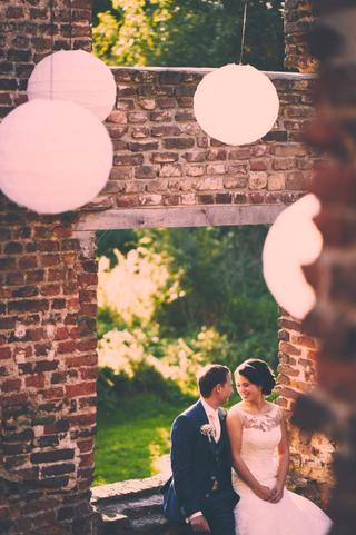 Bruidspaar zit lachend onder roze lampions tegen bakstenen muur, destination wedding fotografie — Trouwshoot Stefan Sege