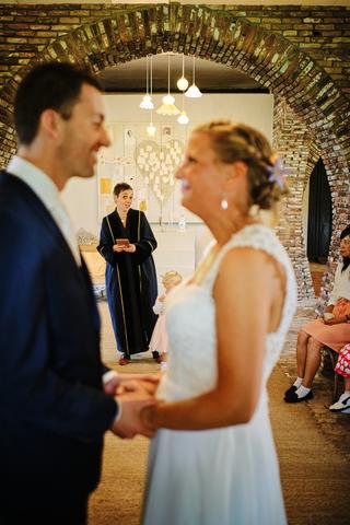 Bruidspaar Menno en Esther wisselen beloften uit onder bakstenen boog, trouwceremonie Hoeve Sparredam Hoevelaken met getuigen