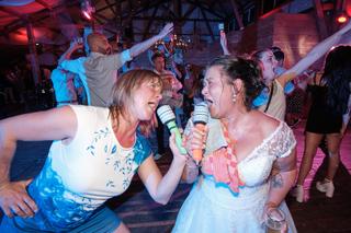 Bruid Raquel zingt karaoke met gast op trouwfeest, industriële feestzaal met neonverlichting, trouwreportage Boerengoed Culem