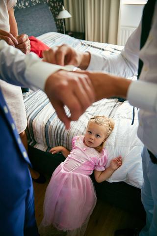 Bruidspaar Sanne en Ferry met bloemenmeisje in roze jurk op hotelbed, intieme trouwvoorbereiding - Trouwshoot Stefan Segers