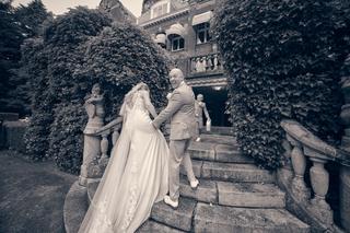 Bruidspaar Kim en Dennis lopen lachend door de met klimop omgeven tuinen van Kasteel De Hooge Vuursche in Baarn - Trouwshoot