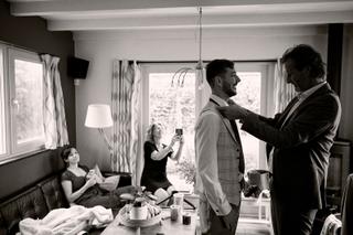 Bruidegom Theron krijgt hulp met stropdas van vader, bruid Milou kijkt toe in woonkamer - Trouwshoot Stefan Segers