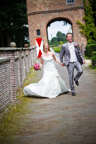 Bruidspaar Jan en Loes rent hand in hand door poort bij slot Zuylen, jurk wapperd in beweging - Trouwshoot Stefan Segers