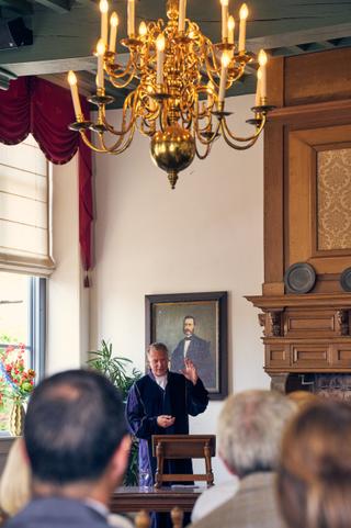 Bruidegom Olav spreekt gasten toe onder gouden kroonluchter in vogeluite zaal tijdens bruiloft met Diliana - Trouwshoot Stefa