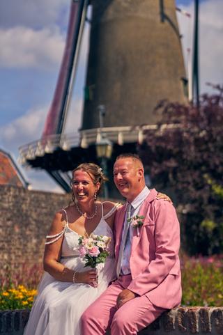 Diliana en Olav stralen van geluk voor de historische molen in IJsselstein, bruidegom in roze pak - Trouwshoot Stefan Segers