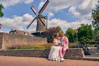 Diliana en Olav zitten verliefd samen op een stenen muurtje met de iconische molen op de achtergrond in IJsselstein - Trouwsh