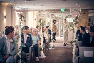 Bruidegoms Robin en partner lopen glimlachend door ceremoniehall Het Wapen van Zoetermeer met gastenheren, groene slingers de
