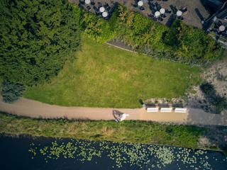 Luchtfoto: bruidspaar Julia en Rens wandelt langs het water bij 't Wapen van Zoetermeer, omgeven door groen en bloeiende wate