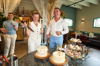Daphne en Edwin snijden samen de bruidstaart aan op Hoeve Kromwijk, omringd door gasten en festijn - Trouwshoot Stefan Segers