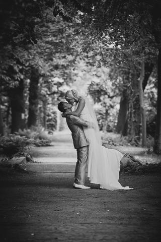 Bruidegom tilt bruid op in bosrijke steeg, romantische moment onder bladerdak - Trouwshoot Stefan Segers