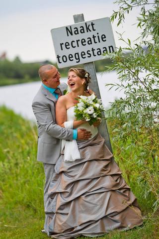 Bruidspaar Corinne en Eelco lachen uitgelaten bij verkeersbord Noord AA met waterplassen en groen op achtergrond - Trouwshoot