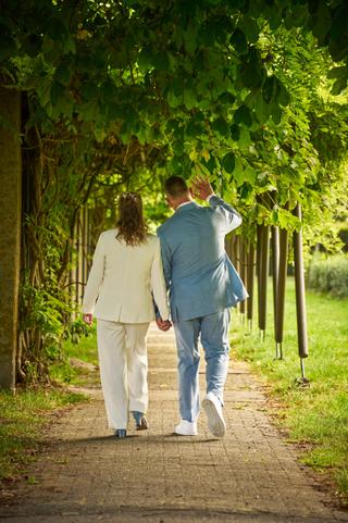 Daphne en Edwin wandelen hand in hand door een groene laan met bladerdak op Hoeve Kromwijk - Trouwshoot Stefan Segers
