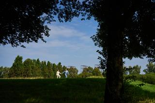 Daphne en Edwin rennen hand in hand door groene weiden onder oude bomen op Hoeve Kromwijk Zoetermeer - Trouwshoot Stefan Sege