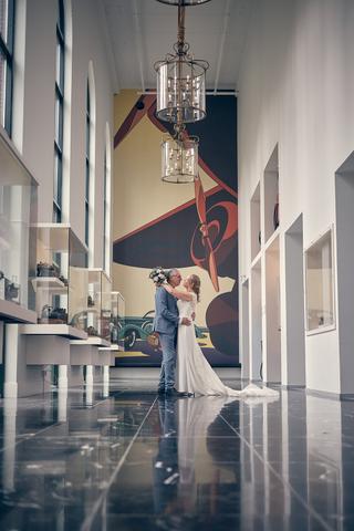 Bruidspaar Herre en Ingeborg kussen in Louwman Museum onder kristallen kroonluchter en klassieke auto's - Trouwshoot Stefan S