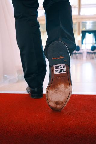 Bruidegom toont zool schoen met 'She's mine!' tekst op rood tapijt bij Stadhuis Zoetermeer - Trouwshoot Stefan Segers