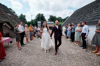 Bruidspaar Simon en Mariëth lopen hand in hand door gasten op Kasteel Essenburgh Hierden, trouwreportage boerderij - Trouwsho