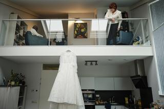 Bruidsjurk hangt in moderne villa, bruidspaar Christa en Gerco kijkt vanaf mezzanine - Trouwshoot Stefan Segers