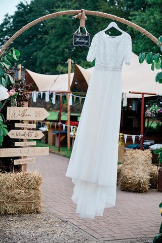Witte trouwjurk van bruid Mariëth hangt aan houten boog met 'Wedding' bordje, rustieke tuinbruiloft - Trouwshoot Stefan Seger